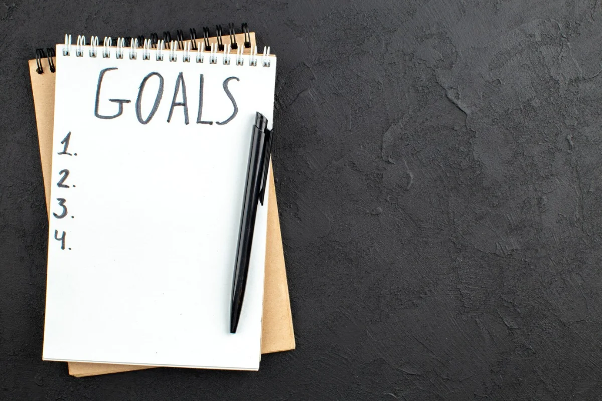A notepad with GOALS written at the top and a list numbered 1 to 4, with a black marker beside it, on a dark textured background.