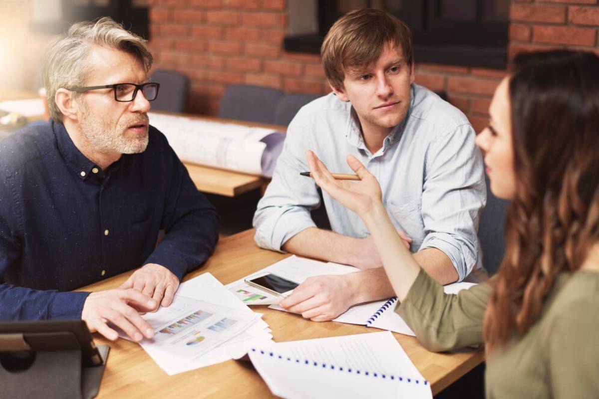 Three colleagues discuss over documents in a casual office setting.