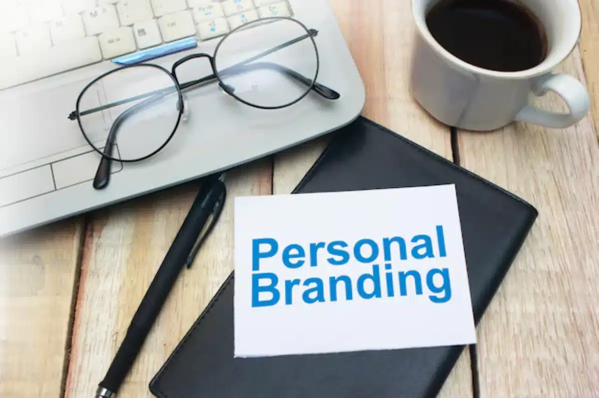 Desk with a laptop, coffee mug, glasses, and a note labelled Personal Branding.