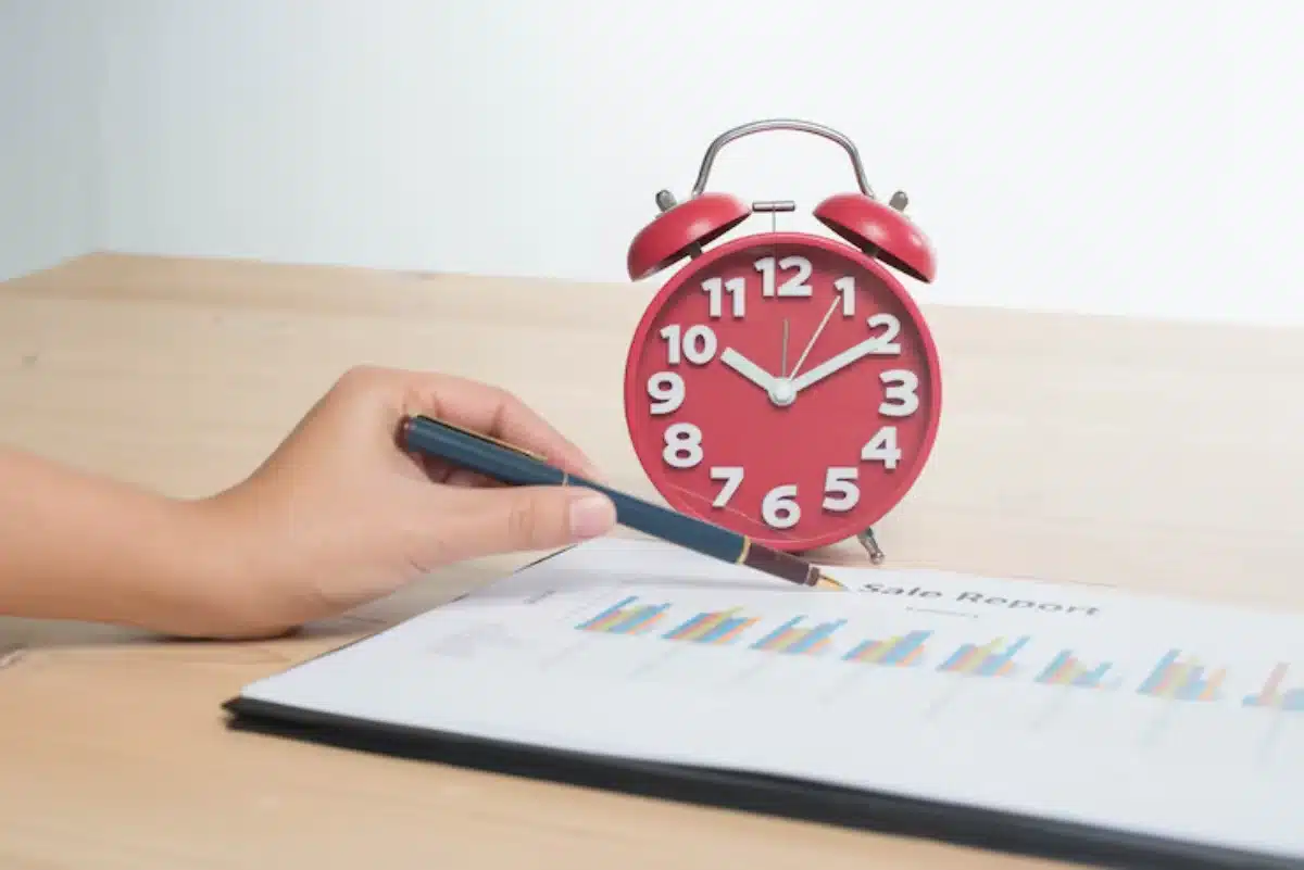 Person reviewing a sales report with a red alarm clock on the table.