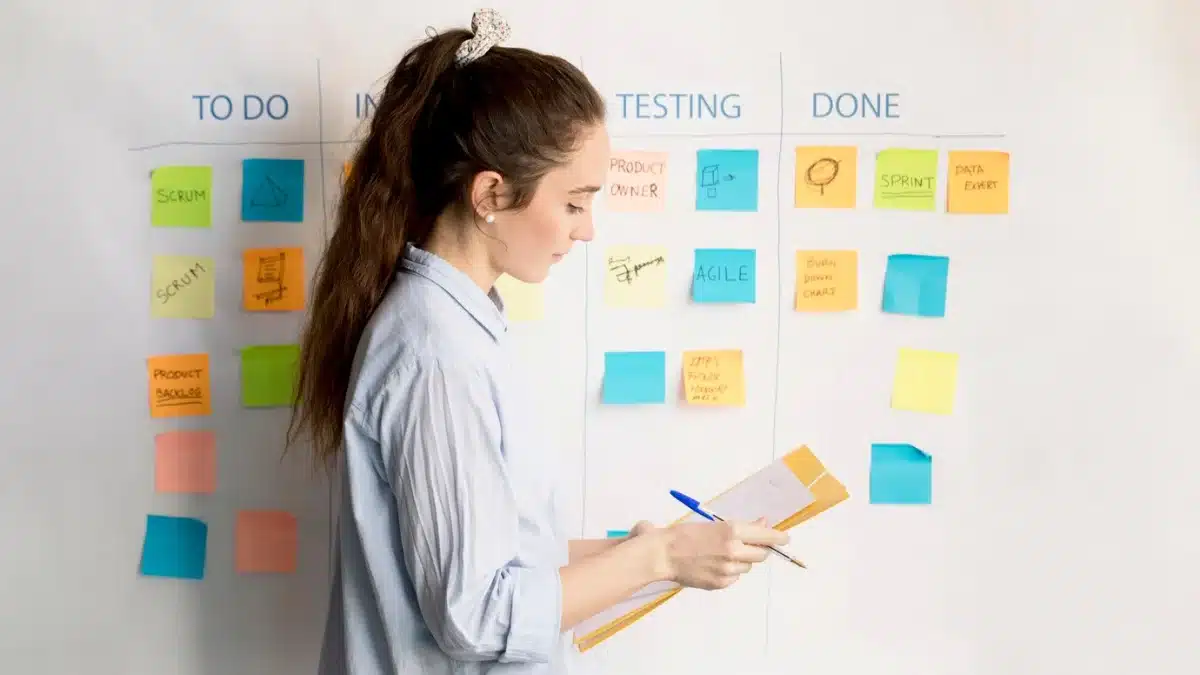 Woman reviewing a project management board with sticky notes labeled under categories like To Do Testing, and Done.