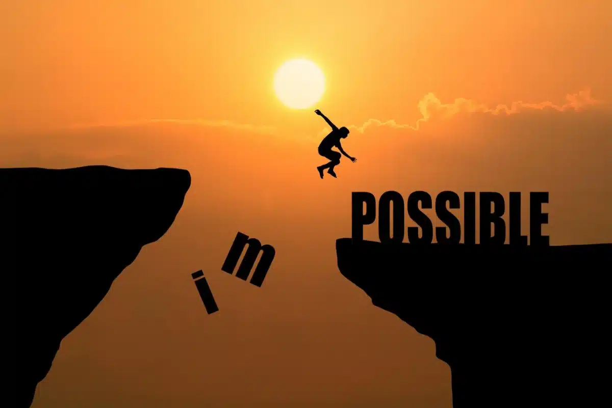 Silhouette of a person jumping between cliffs with the word POSSIBLE completing as they leap; sunset background.