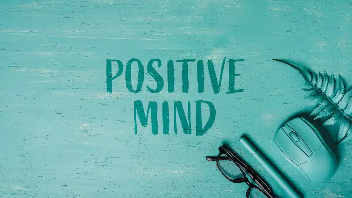 Teal desktop with POSITIVE MIND text, a mouse, glasses, and a fern leaf on the side.