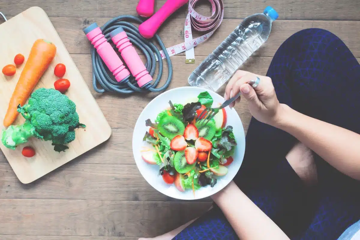 Top view of a person eating a colourful salad, surrounded by workout gear and fresh vegetables.